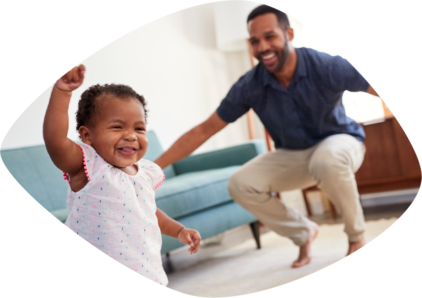 Un papá afroamericano y su hijita se están riendo y están brincando en la sala de su casa